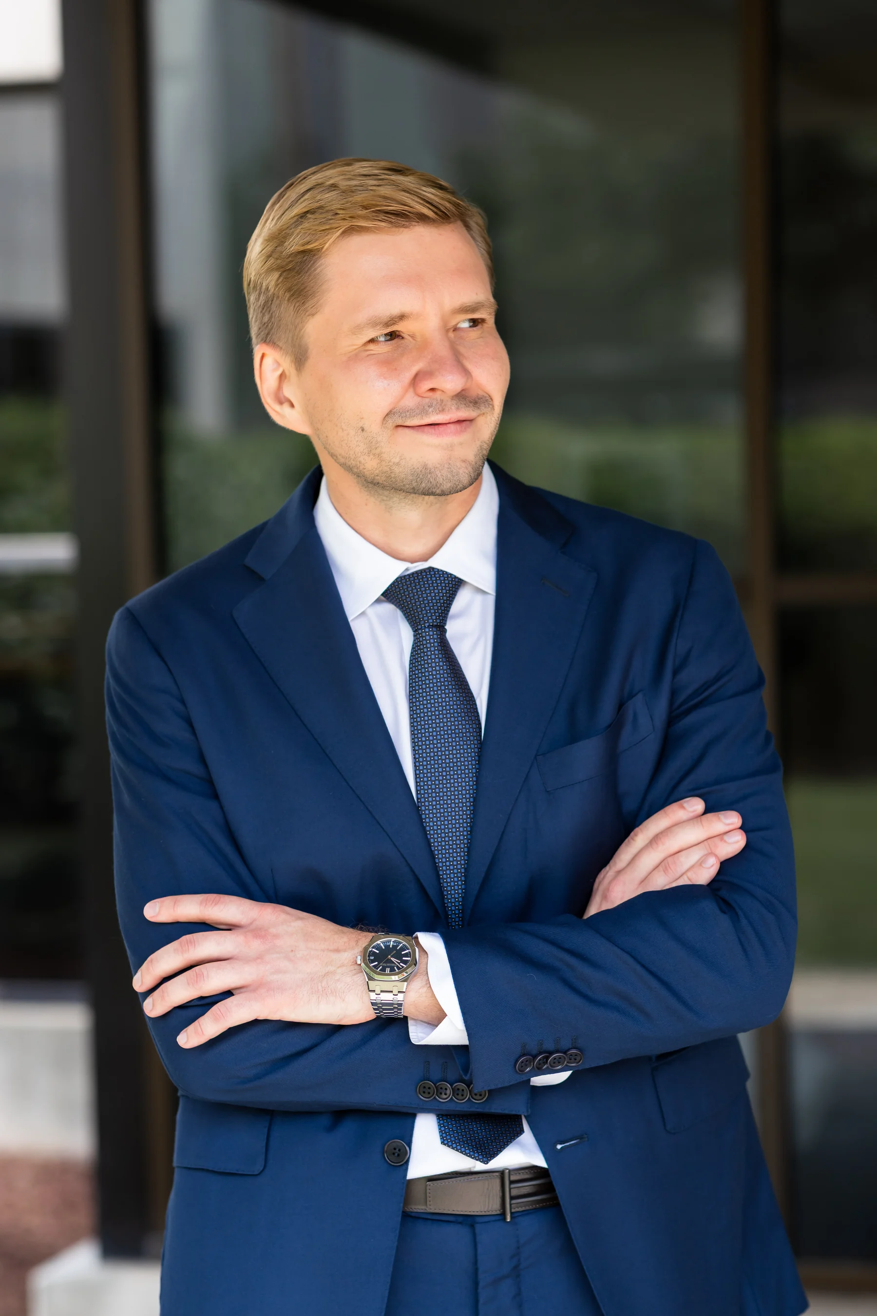 Dr. Yaranov in a navy suit and tie, arms crossed, standing outdoors in front of a glass building