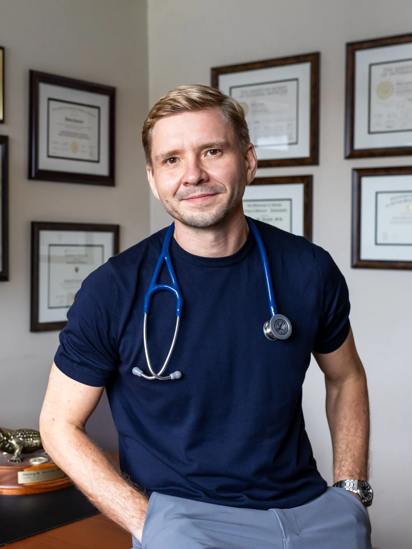 Dr. Yaranov in his office in front of his framed diplomas, a blue stethoscope around his neck, smiling at the camera