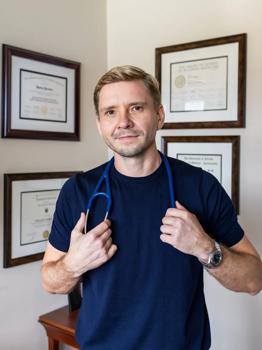 Dr. Yaranov in a navy shirt with a stethoscope around his neck, hands on it, smiling