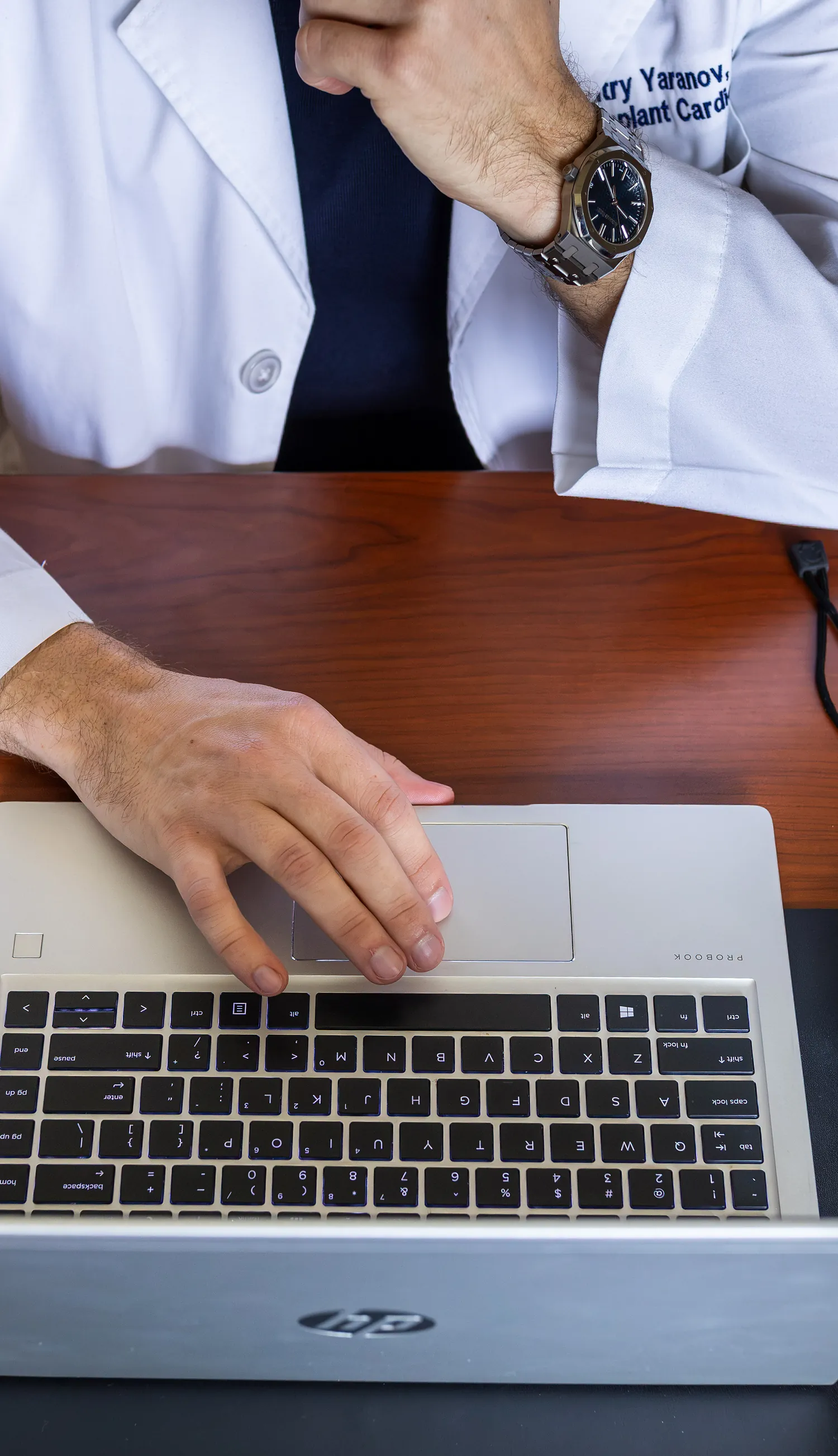 Overhead view of Dr. Yaranov's hand on a laptop trackpad at his desk, his other hand resting at his chin