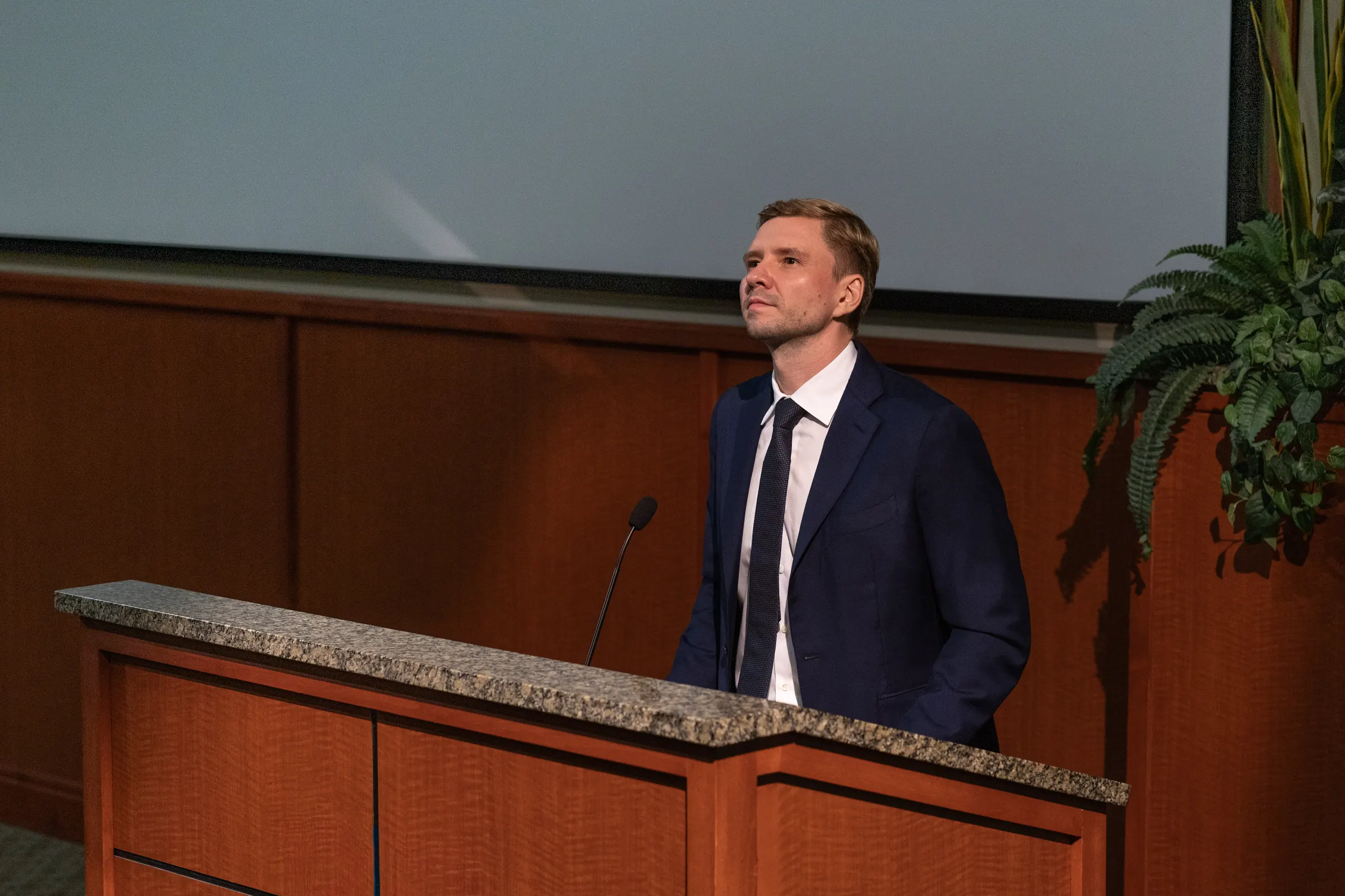 Dr. Yaranov at a lectern in a lecture hall, looking up at the screen